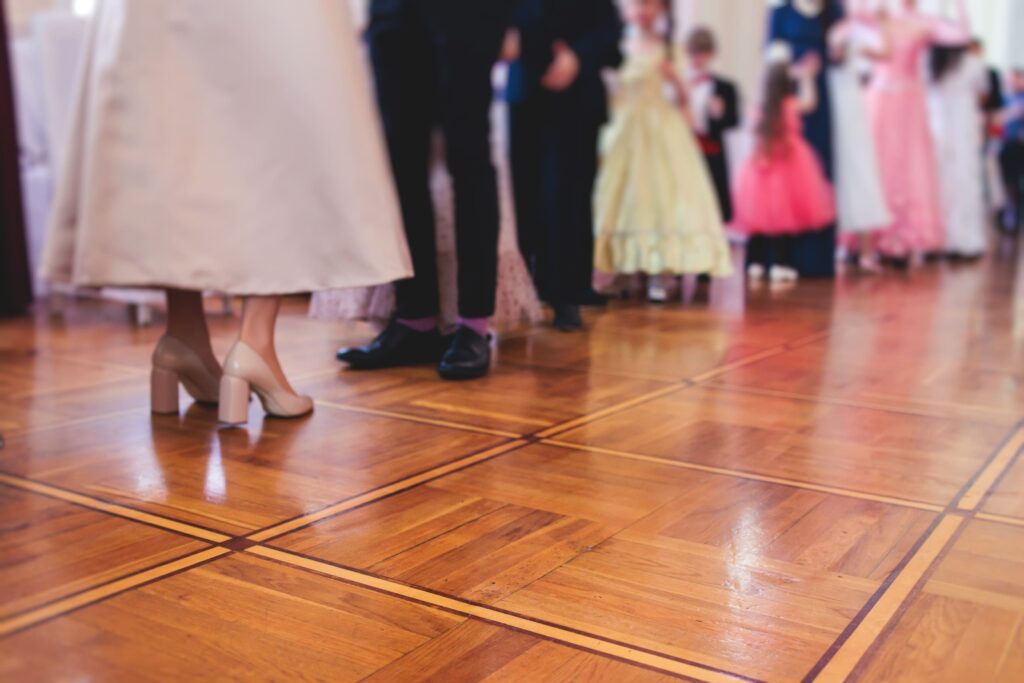 people in formal attire standing on a polished parquet dance floor during a social event.