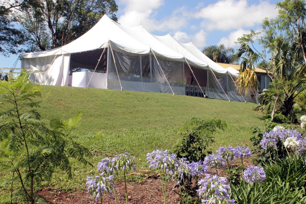 A large, white peak-style marquee tent with clear side panels situated on a grassy hill